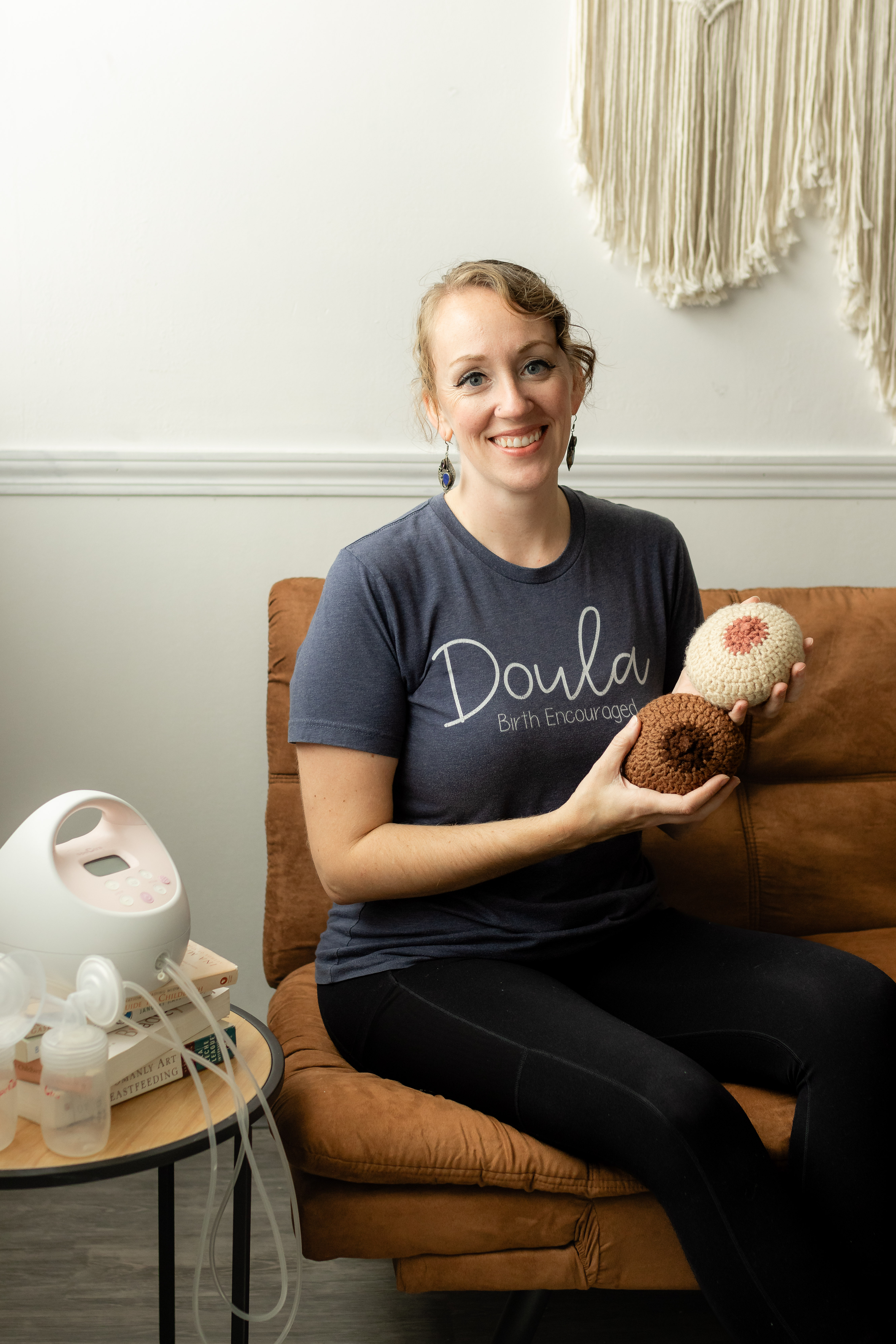 Ronae Cleland, smiling warmly, holding breast models and a pump, ready to educate families as a certified lactation consultant.