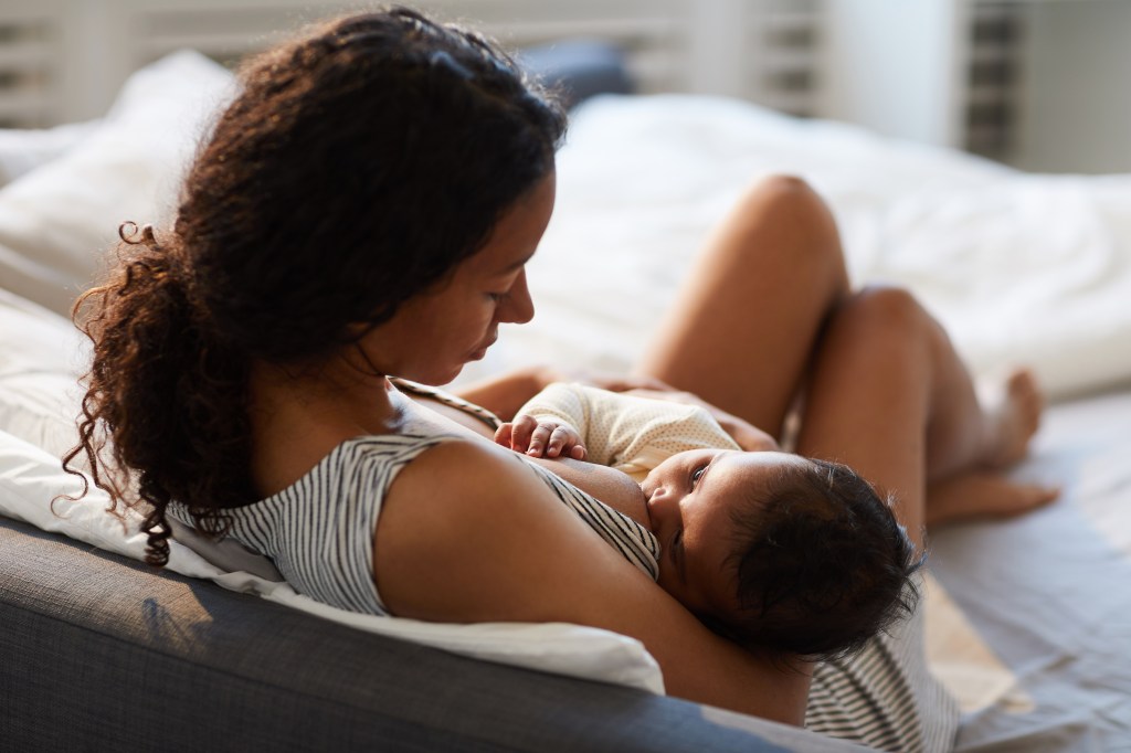 Young mother breastfeeding baby on a bed with white sheets Young mother breastfeeding her baby on a bed with white sheets, creating a peaceful and nurturing bonding moment.