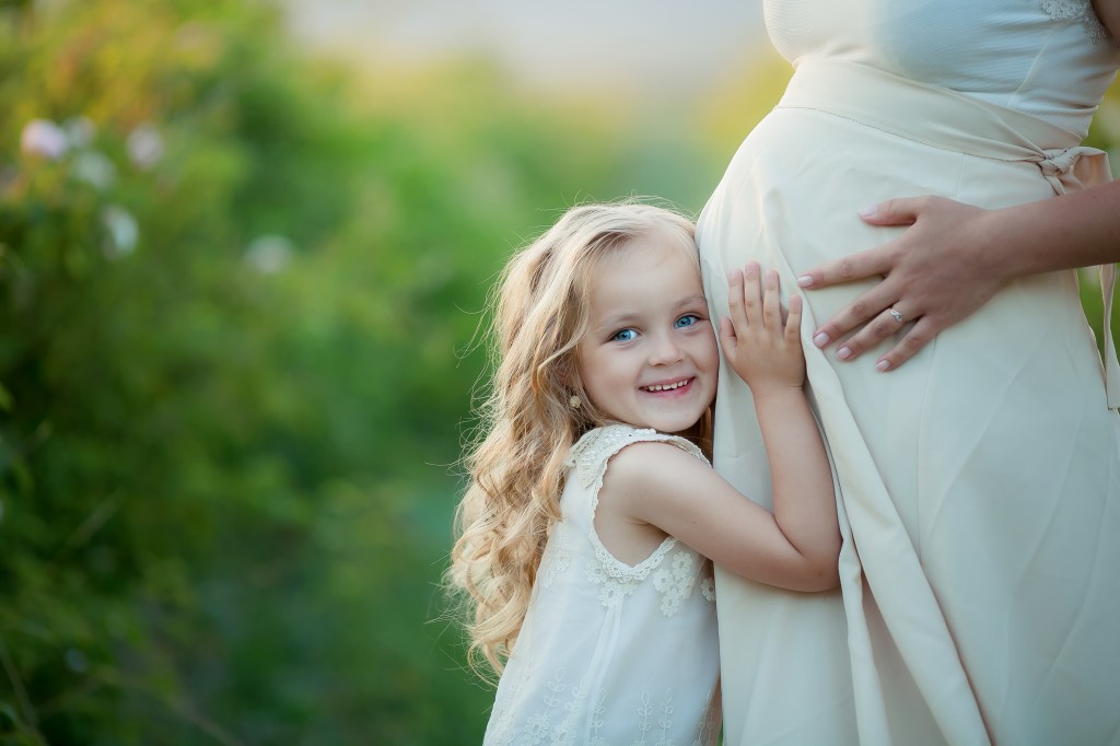 Young child hugging her pregnant mother's stomach A young girl smiles as she lovingly hugs her pregnant mother's belly.